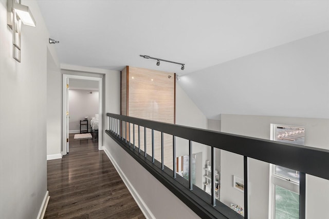 hall with dark wood-style floors, rail lighting, baseboards, and lofted ceiling