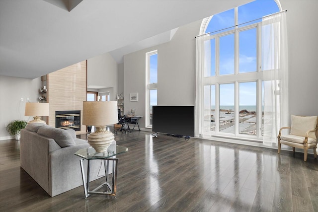 living area with a tiled fireplace, a towering ceiling, and dark wood-style flooring