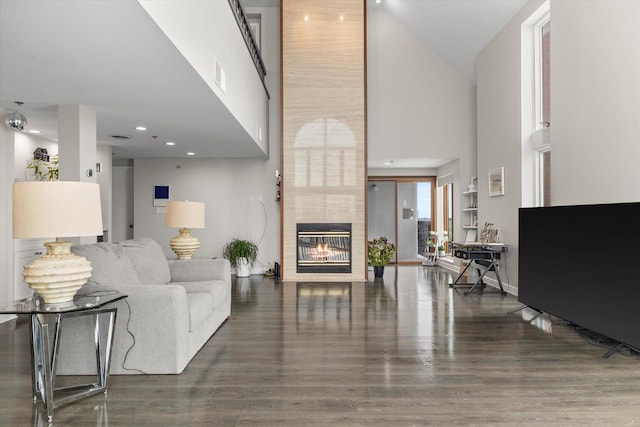 living area featuring wood finished floors, visible vents, baseboards, a high ceiling, and a tiled fireplace