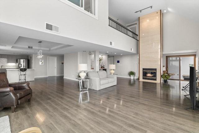 living room with visible vents, a raised ceiling, wood finished floors, and a tiled fireplace