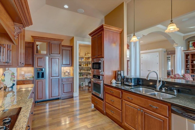 kitchen featuring a sink, ornate columns, stainless steel appliances, arched walkways, and hanging light fixtures