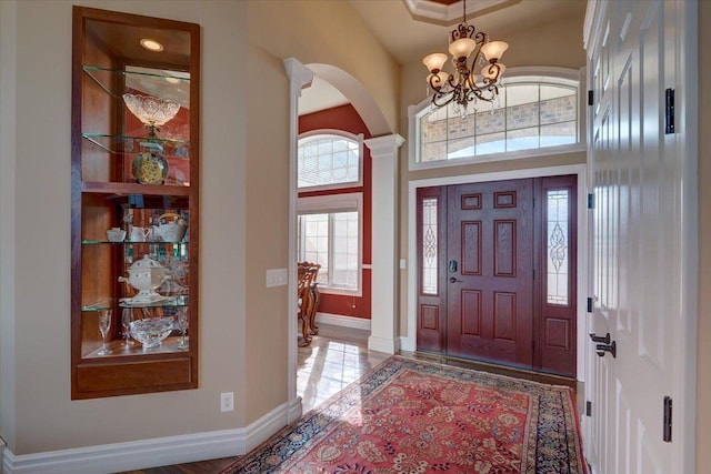 entrance foyer with baseboards, arched walkways, a towering ceiling, and a chandelier