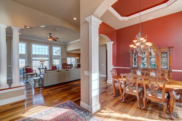 dining area featuring wood finished floors, a ceiling fan, ornate columns, arched walkways, and ornamental molding