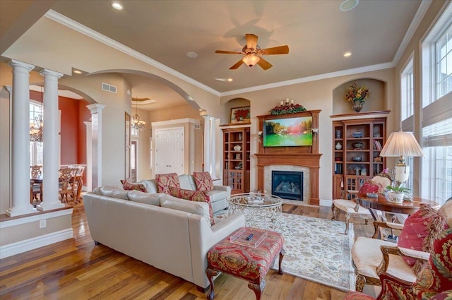 living room featuring wood finished floors, arched walkways, a fireplace, ceiling fan, and ornate columns