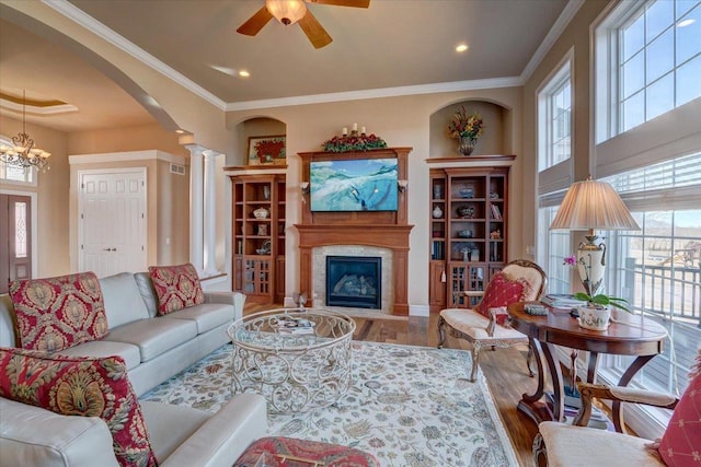 living room featuring ornamental molding, ceiling fan with notable chandelier, wood finished floors, arched walkways, and a glass covered fireplace