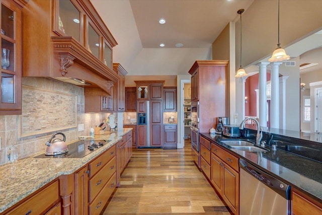 kitchen with a sink, stainless steel appliances, light stone countertops, and decorative light fixtures