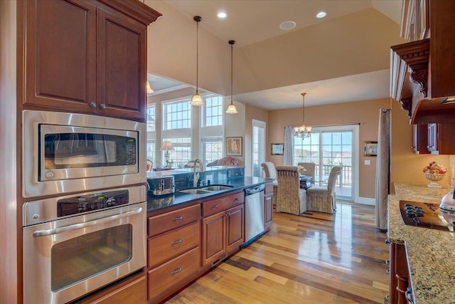 kitchen with light stone countertops, light wood finished floors, a sink, appliances with stainless steel finishes, and a notable chandelier