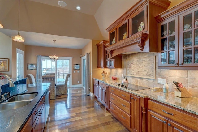 kitchen with light wood finished floors, decorative light fixtures, brown cabinets, black electric cooktop, and a sink