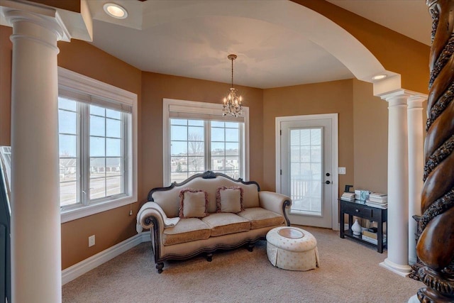 living area featuring baseboards, arched walkways, ornate columns, and light carpet