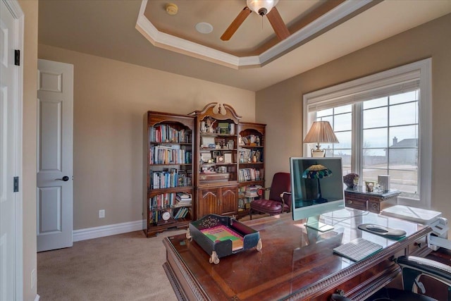 office space with a ceiling fan, a tray ceiling, crown molding, baseboards, and light colored carpet