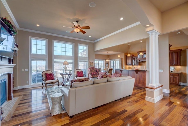 living area featuring light wood finished floors, ornamental molding, ceiling fan, and decorative columns