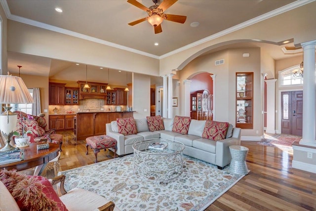 living room featuring visible vents, crown molding, ornate columns, wood finished floors, and a ceiling fan