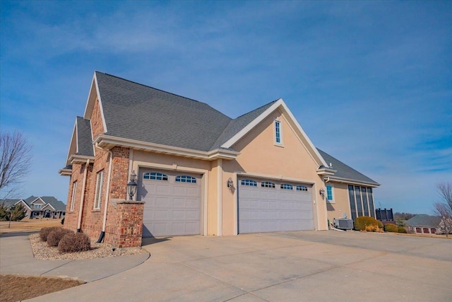 view of side of property featuring roof with shingles, driveway, an attached garage, stucco siding, and brick siding