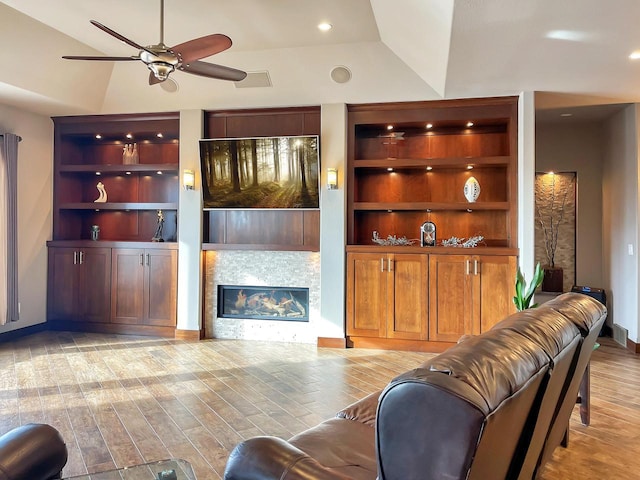 living room featuring built in features, lofted ceiling, light wood-style flooring, a fireplace, and a ceiling fan