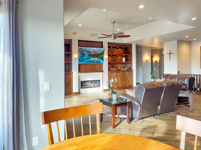 living area with built in shelves, ceiling fan, recessed lighting, wood finished floors, and a glass covered fireplace