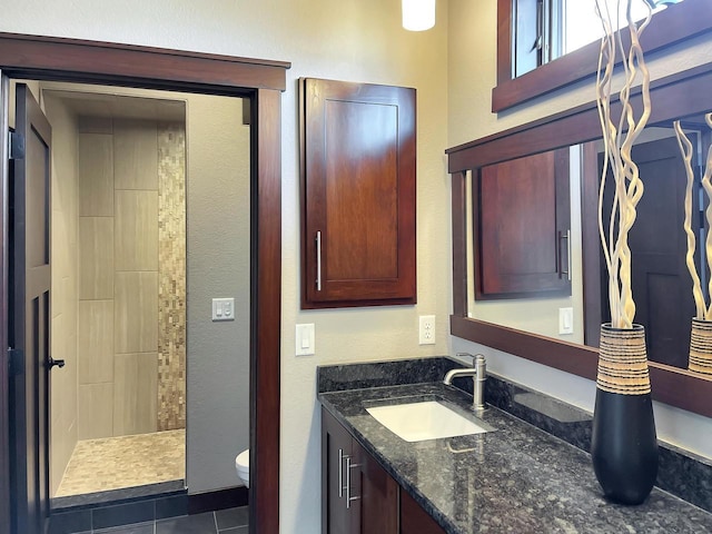 bathroom with a tile shower, toilet, and vanity