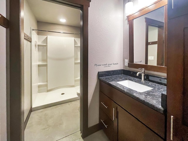 full bath featuring toilet, a stall shower, vanity, and a textured wall