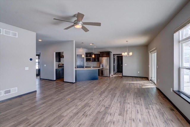 unfurnished living room featuring ceiling fan with notable chandelier, wood finished floors, visible vents, and a sink