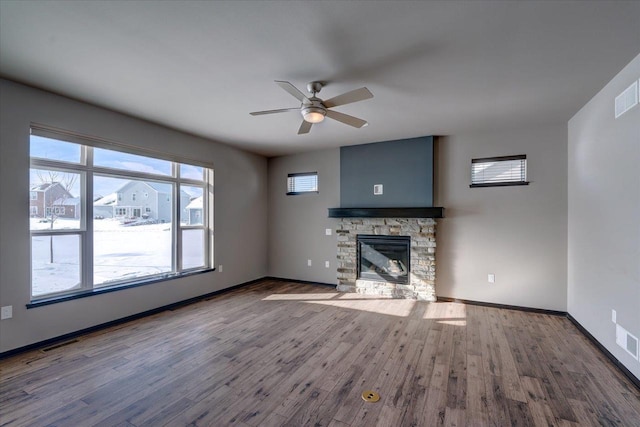 unfurnished living room featuring wood finished floors, a ceiling fan, baseboards, visible vents, and a stone fireplace