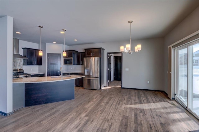 kitchen with a sink, decorative backsplash, stainless steel appliances, wall chimney exhaust hood, and a notable chandelier