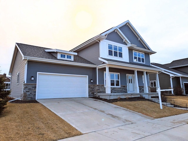 craftsman house featuring driveway, covered porch, a front lawn, a garage, and stone siding