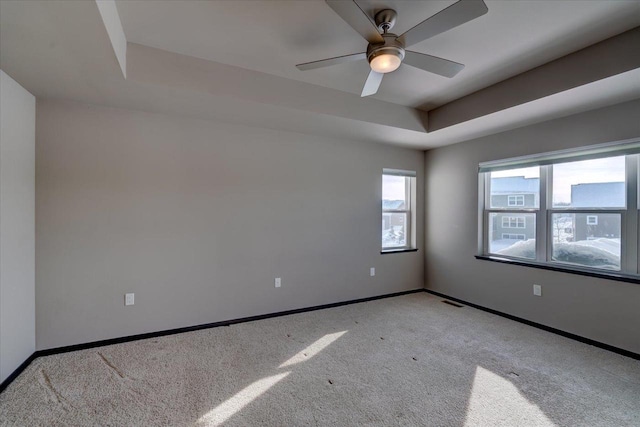 spare room with visible vents, baseboards, a tray ceiling, light carpet, and a ceiling fan