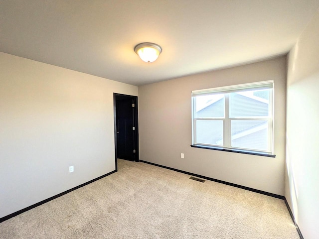 empty room featuring light colored carpet, visible vents, and baseboards