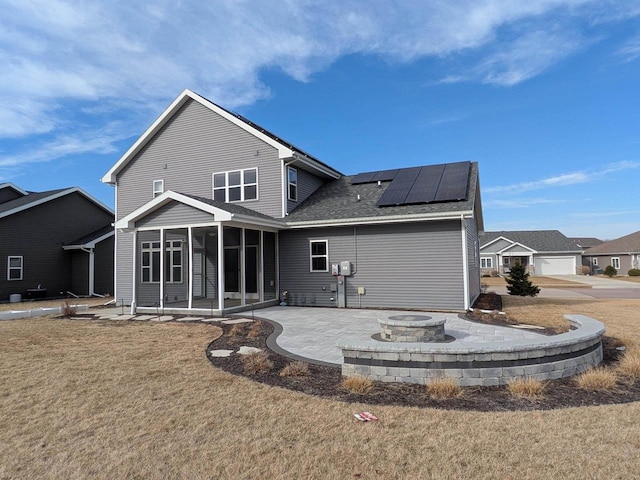 back of property with solar panels, an outdoor fire pit, a lawn, a sunroom, and a patio area