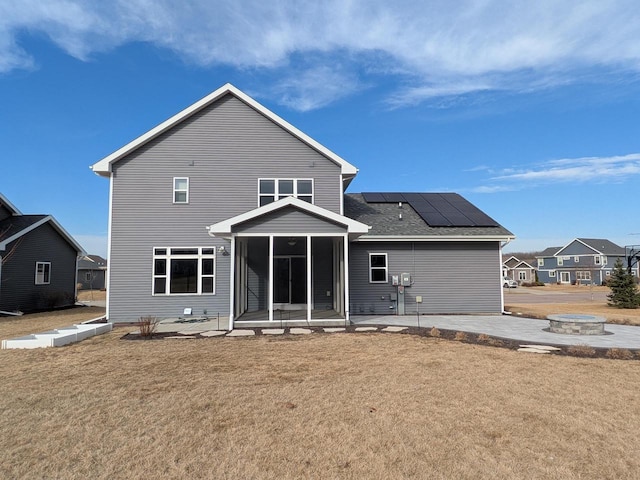 back of property with a patio, a yard, roof mounted solar panels, and a sunroom