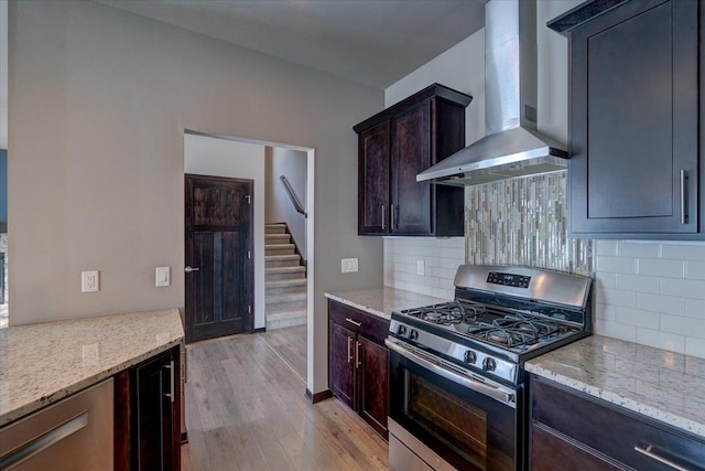 kitchen with wall chimney exhaust hood, stainless steel range with gas stovetop, light wood-type flooring, and light stone countertops