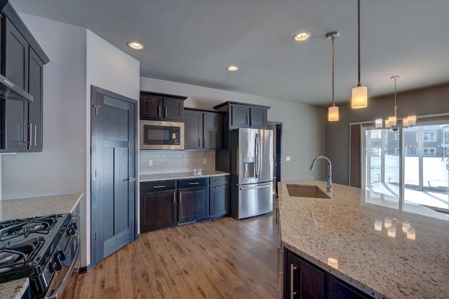 kitchen featuring decorative backsplash, an inviting chandelier, light wood-style floors, stainless steel appliances, and a sink