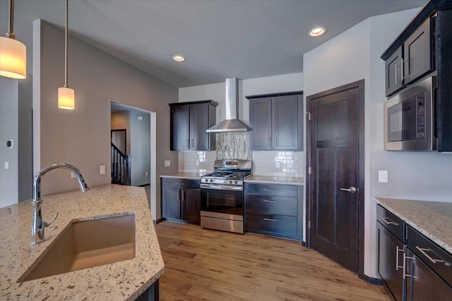 kitchen with light stone countertops, stainless steel appliances, wall chimney exhaust hood, and a sink