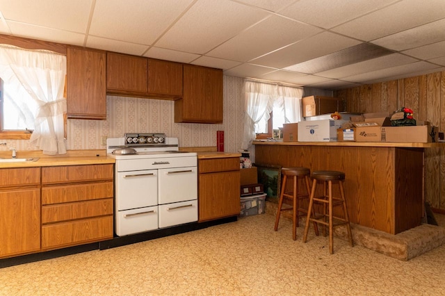 kitchen featuring brown cabinets, a sink, wallpapered walls, range with two ovens, and light countertops