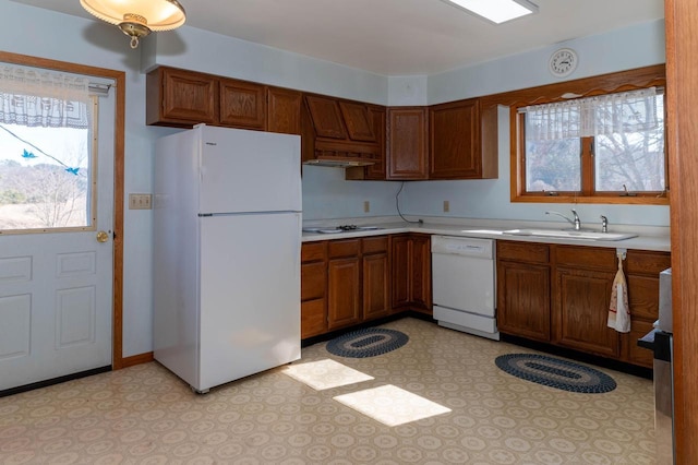 kitchen with brown cabinetry, white appliances, light countertops, and a sink