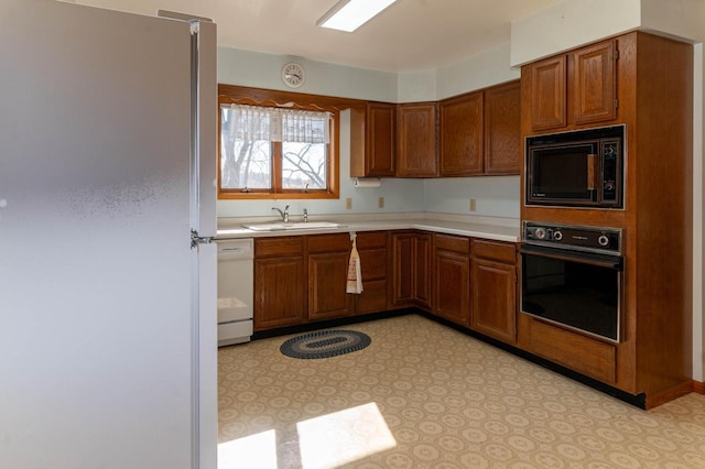 kitchen featuring black appliances, light countertops, brown cabinets, and a sink