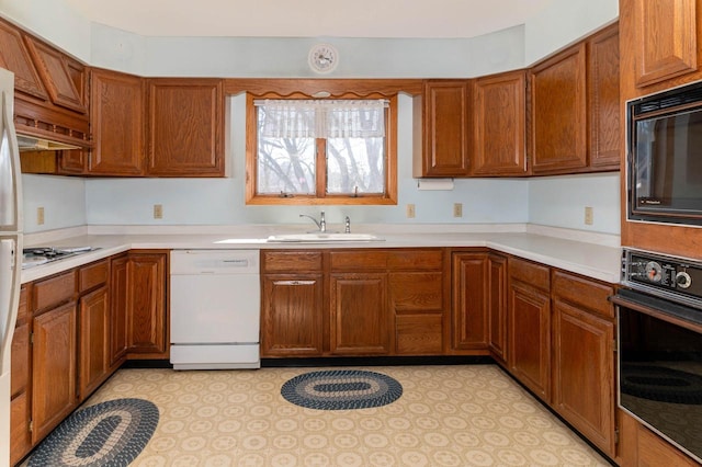 kitchen featuring brown cabinets, black appliances, light countertops, and a sink