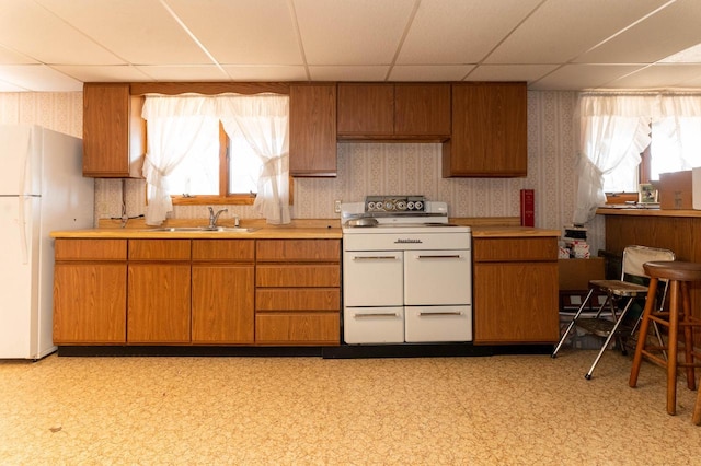 kitchen with white appliances, light floors, wallpapered walls, a sink, and light countertops