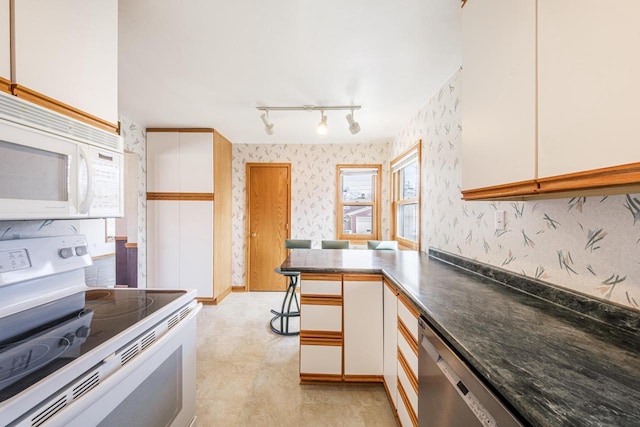 kitchen with dark countertops, white cabinetry, white appliances, a peninsula, and wallpapered walls