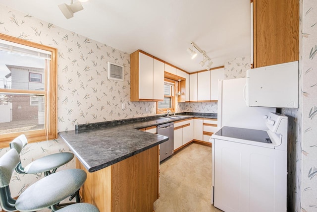 kitchen featuring washer / clothes dryer, dark countertops, a peninsula, wallpapered walls, and dishwasher