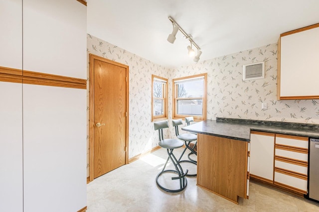 kitchen with dark countertops, a breakfast bar area, dishwasher, and wallpapered walls