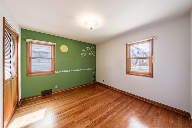 unfurnished room with light wood-style floors, visible vents, and baseboards