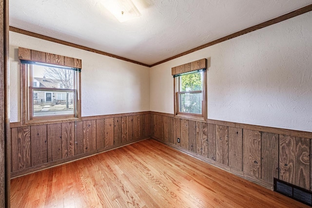 unfurnished room featuring a wainscoted wall, visible vents, ornamental molding, wood walls, and light wood-type flooring