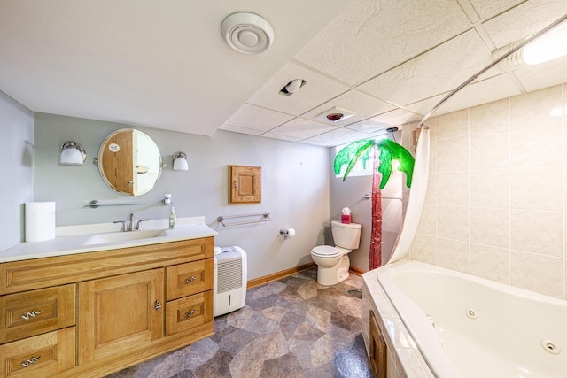 bathroom featuring toilet, a combined bath / shower with jetted tub, a drop ceiling, baseboards, and vanity