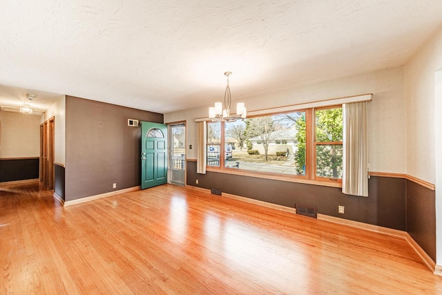 empty room featuring visible vents, a textured ceiling, light wood-style floors, an inviting chandelier, and baseboards