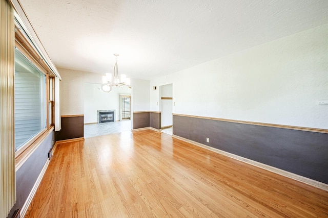 unfurnished living room featuring a glass covered fireplace, baseboards, a notable chandelier, and light wood-style flooring