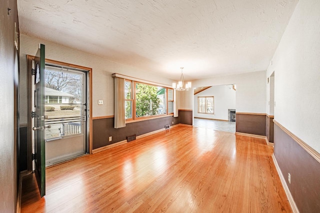 empty room featuring visible vents, a chandelier, wainscoting, light wood-style floors, and a textured ceiling