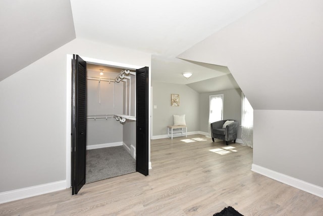 additional living space featuring light wood finished floors, baseboards, and vaulted ceiling