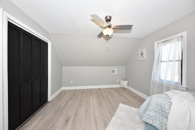 bedroom featuring visible vents, baseboards, light wood-type flooring, vaulted ceiling, and a closet