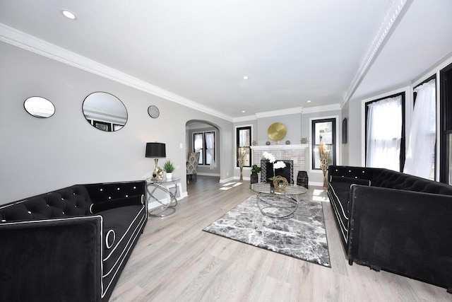 living room featuring wood finished floors, baseboards, arched walkways, ornamental molding, and a brick fireplace