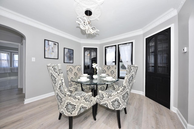 dining area featuring light wood finished floors, baseboards, a chandelier, ornamental molding, and arched walkways